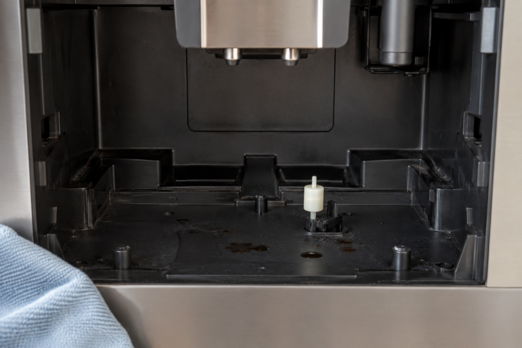 The empty niche where the drip tray sits, with a small float contact and a few dried coffee spots on its floor.